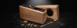 Un plan de conception détaillé pour l'enceinte ASA Grand Monitor Pro, avec des prototypes de boîtiers en bois massif et des outils de sculpteur sur un bureau d'atelier d'ébenisterie en France.